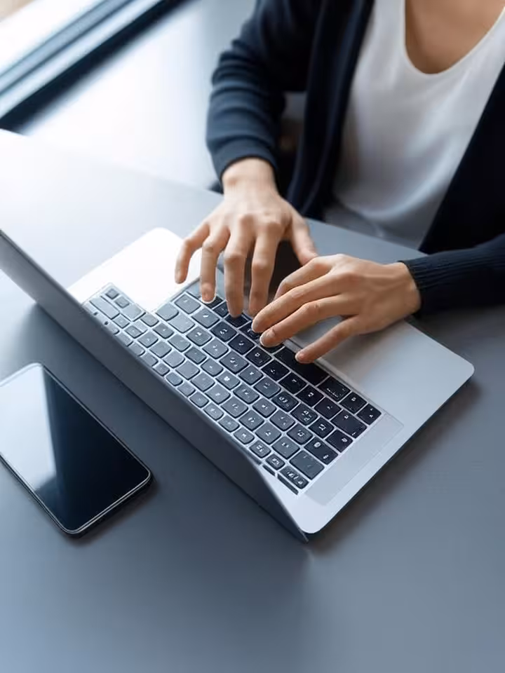 Woman's hands typing on laptop creating dating profile, coffee shop setting, soft natural window lig